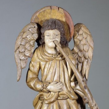 Ангел аналогичен по выполнению ангелу с трубой вправо вниз, но по композиции имеет обратный перевод.
На голове - нимб. Лицо вырезано удлиненными, с резкорельефными чертами. Одежды на фигуре образуют много пышных складок.