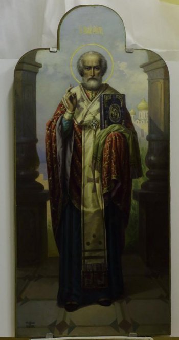Изображен св. Николай Мирликийский в рост, в священнической одежде, с евангелием на левой руке. Фон светлый, с изображением храма справа и колонн.