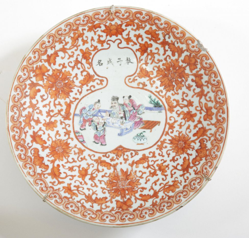 Блюдо круглое, с наружной стороны расписано красным цветочным орнаментом в китайском стиле; на дне (зеркале), в белом фигурном резерве, изображена жанровая композиция из китайской жизни.