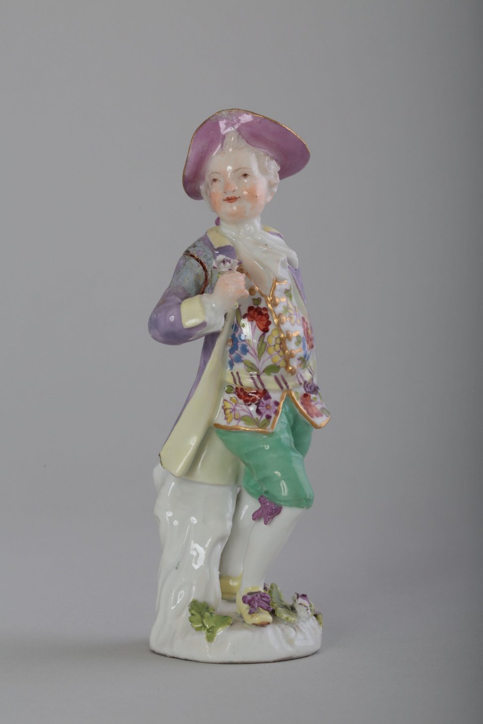 Фигура мужчины (маркиза?) в костюме XVIII века. Одет мужчина в сиреневый камзол, зеленые панталоны до колен, на голове - сиреневая шляпа. В правой руке держит цветок.