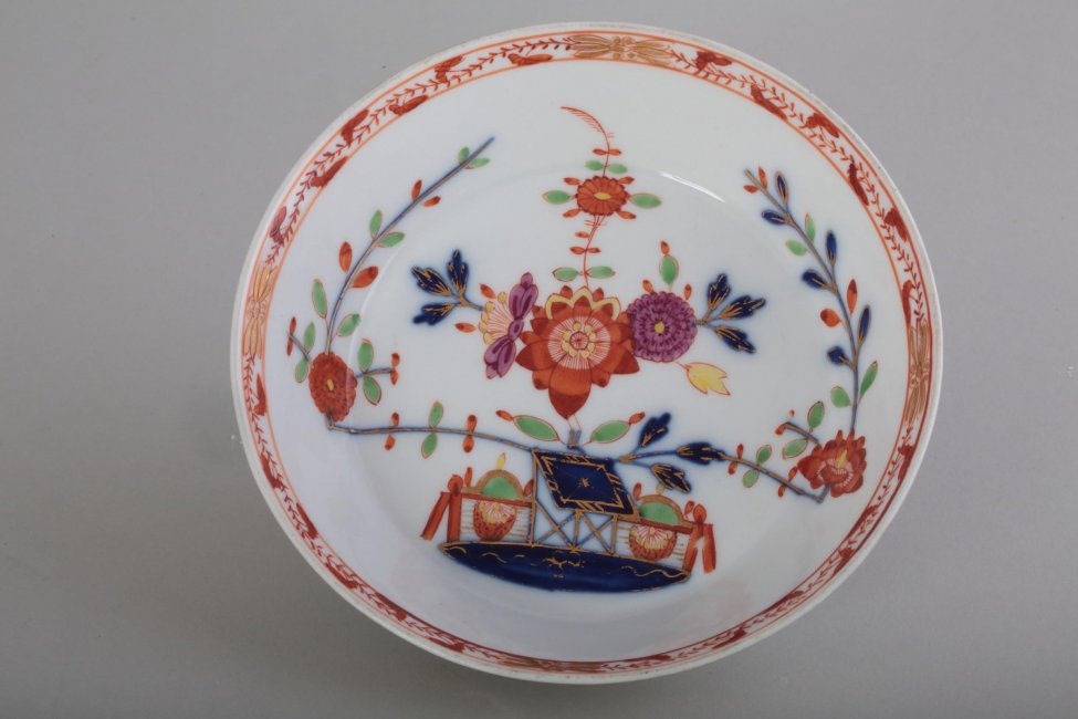 Блюдце круглое, с прямым бортом; на зеркале стилизованное изображение цветов в китайском стиле; по верхнему краю борта орнаментальная кайма
