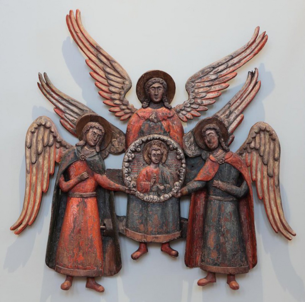 Композиция состоит из трех архангелов; на среднем, стоящем прямо, находится рельефное в обрамлении изображение благословляющего Эммануила; это изображение поддерживают обращенными друг к другу руками два архангела по сторонам; их другие руки подняты на грудь. Архангел справа изображен в небольшом повороте влево. Архангел слева имеет некоторый поворот вправо. На архангелах изображено по две одежды, окрашенных в красный и синий цвета. У крайних архангелов некоторые одежды вырезаны отошедшими с боков на стороны. Изображения архангелов исполнены в ограниченное число плоскостей. Отдельно вырезанные крылья окрашены в серый цвет.