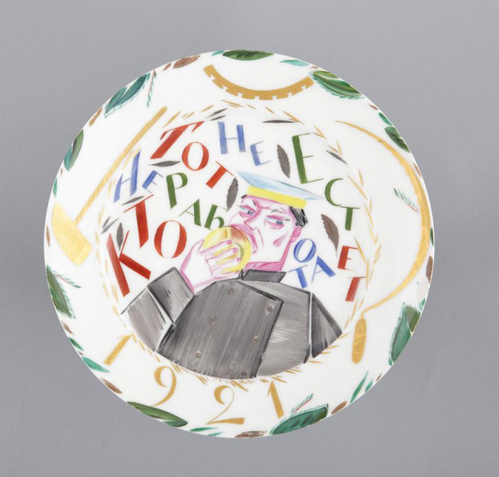 На церкале поясное изображение мужчины, жующего булку и надпись: «Кто не работает тот не ест»; на полях золотом - серп, молот, шестерня и дата «1921»
