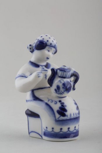 Фигурка сидящей на табурете женщины,  левой рукой она держит на коленях чайник, в правой - кисть