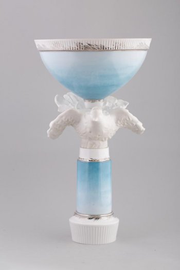 Полусферической формы в виде чаши, на высокой цилиндрической  ножке с фигурой белого летящего голубя; основание круглое, книзу сужается; наружная часть вазы и ножка голубого цвета; край чаши украшен золотым пояском.