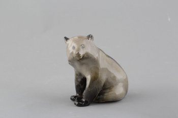 Фигура сидящего серо-черного медведя; глаза, уши, лапы - чёрные. Он сидит опираясь на передние лапы, задняя левая лапа - между двумя передними.  Голова в 3/4 повороте вправо.
