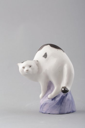 Фигура  белой с чёрными пятнами кошки с выгнутой спиной и распущенным хвостом. Голова в 3/4 развороте вправо. Основание высокое, неправильной округлой формы.