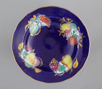 Тарелка глубокая синяя, с волнистым краем, с росписью четырех композиций из плодов, ягод и листьев на белом фоне; части изображений, заходящие на синий фон тарелки - исполнены позолотой.