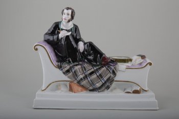 Чернильный прибор, изображающий А.С.Пушкина в домашней обстановке, облокотившегося на спинку кушетки, пишущего на листе бумаги, положенном на колено правой ноги.