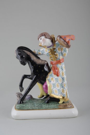 На прямоугольном основании 2-х фигурная композиция: черного коня, присевшего на задние копыта и  сидящего сверху юноши, одетого в русский костюм.