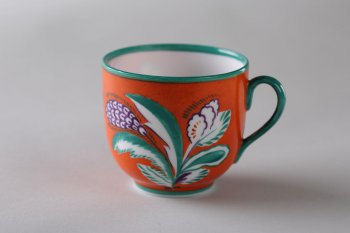 Чашка красная, край и ручка - зеленые. На тулове с двух сторон  роспись сильно стилизованными цветами с бело-зелеными листьями.