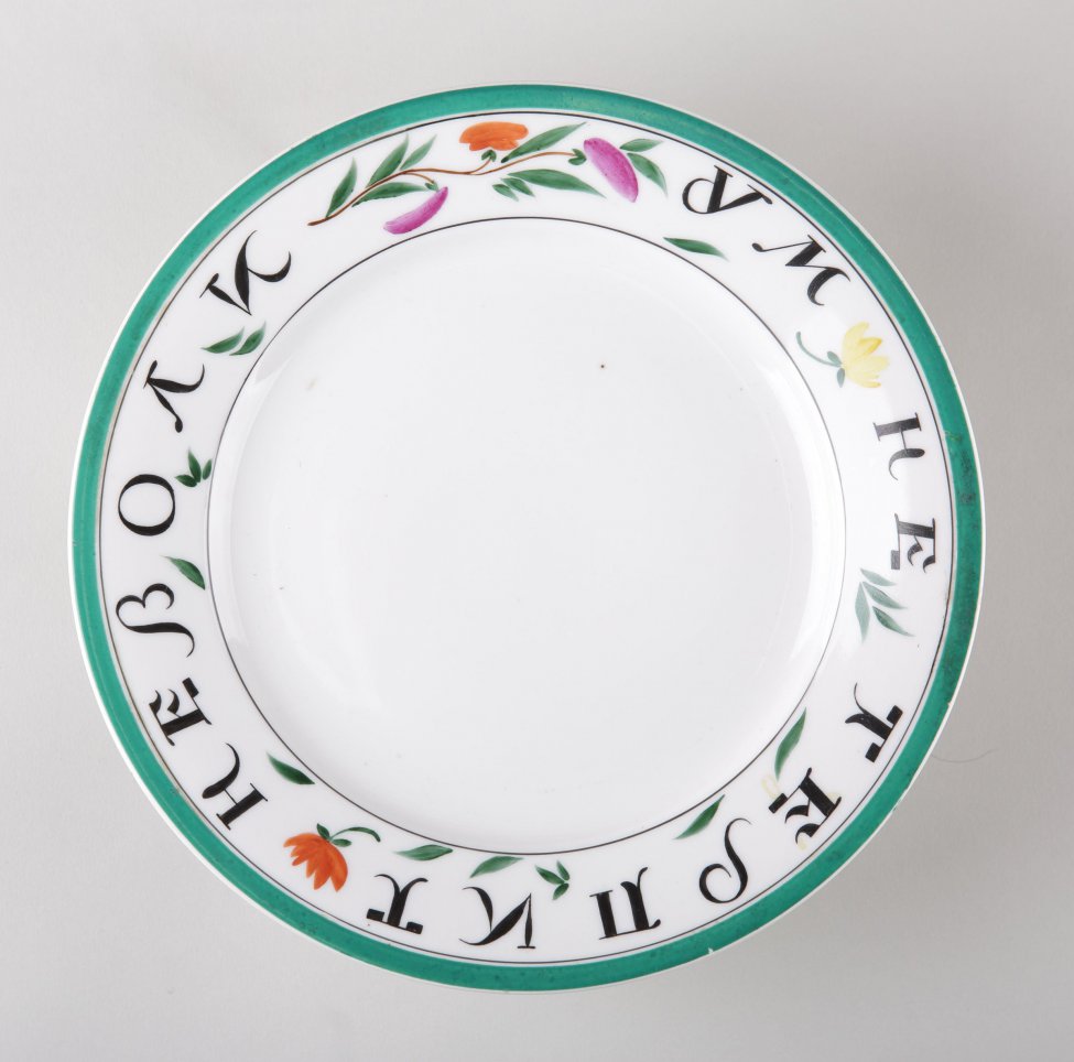 По борту тарелки черная надпись:" ум не терпит неволи", между словами и над словами изображены цветы и листья: цветы - малиновые, красные и желтые. По краю тарелки зеленая кайма.