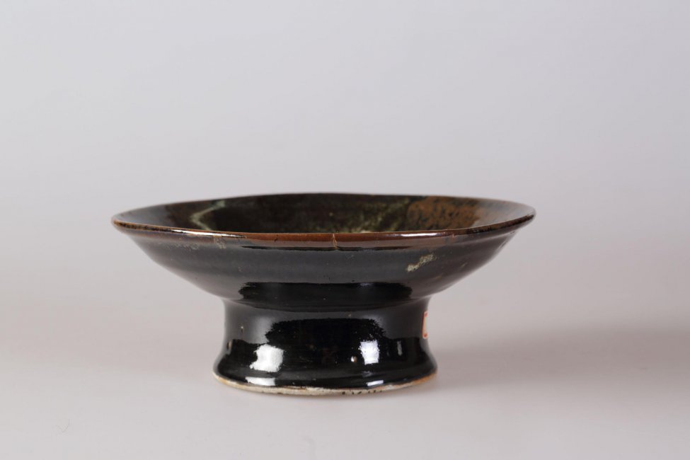 Тарелка в форме вазочки на высокой кольцевой ножке, снаружи черная, внутри темно-коричневая, с тремя светлыми пятнами.