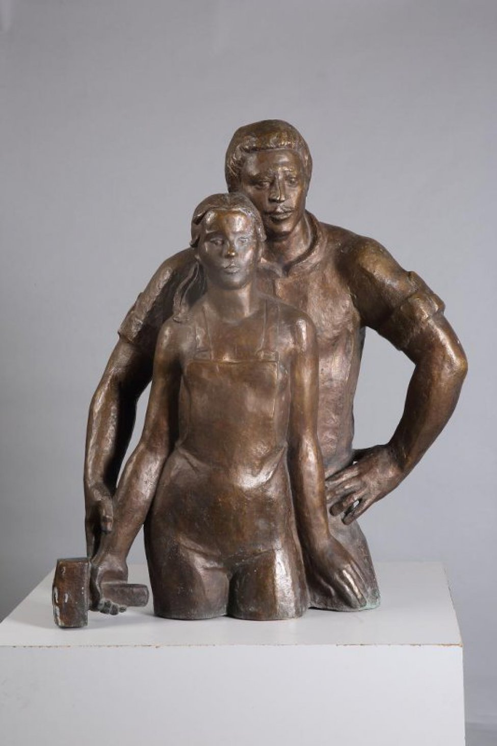 Скульптурная композиция из двух фигур изображенных победренно. На первом плане - молодая женщина в рабочем комбинезоне, в правой руке скульптурный молоток, левая рука лежит на бедре мужчины. Волосы, зачесаны на прямой пробор и убраны за уши, лежат на правом плече. На втором плане - молодой мужчина, стоящий за спиной женщины, его правая рука поддерживает руку женщины с молотком. Левая рука мужчины упирается в бедро. Щекой мужчина прижимается к волосам женщины.