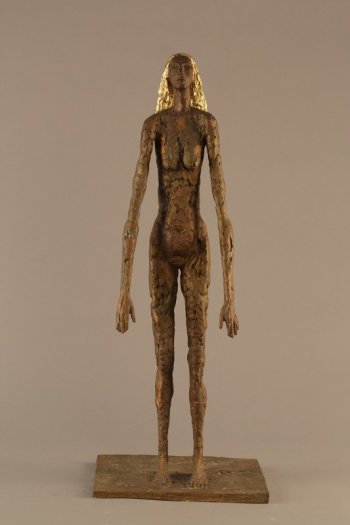 На прямоугольном основании изображена в полный рост стилизованная фигура обнаженной женщины с золотистыми волосами до плеч. Руки опущены и слегка вытянуты вперед, голова слегка поднята вверх. Поверхность скульптуры фактурная, имитирующая лепку из пластилина.