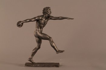На прямоугольном плинте изображена мужская обнаженная фигура в рост в движении. Мужчина стоит на пальцах левой ноги,  правая нога согнута в колени и поднята, левая рука вытянута горизонтально вперед, правая рука с диском отведена назад.