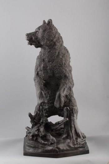 Изображен в рост, вствший на задние лапы медведь. Голова медведя развернута на 3/4 вправо, пасть открыта. Постамент имитирует часть пня: на нем елки, сучья.
