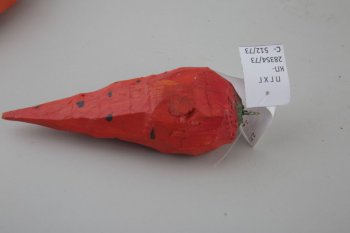 Обобщенное изображение моркови оранжево-красного цвета, с черными точками. Наеерху зеленое пятно с треугольным креплением.