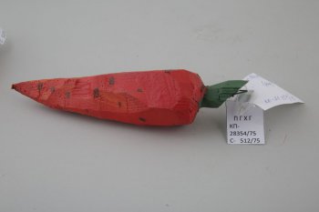 Обобщенное изображение моркови оранжево-красного цвета с оранжевыми разводами, с темно-коричневыми точками. Сверху короткая зеленая ветка, срезанная под углом. К ней прикреплено треугольное металлическое крепление.