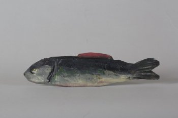 Обобщенное изображение рыбы с одним плавником на спине, туловище - от черного до серого, с зелеными мазками, брюшко светло-серое с розовым. Глаз выполнен в виде сквозного отверстия и подкрашен зеленой краской. Жабры с обеих сторон обозначены вырубкой.