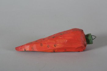 Обобщенное изображение моркови темно-оранжевого цвета с темно-коричневыми точками. Сверху короткая зеленая веточка, на которой треугольное крепление.  На одной из сторон у веточки углубление в древесине, окрашенное в общий цвет.