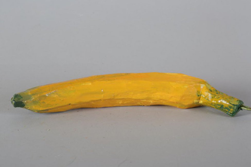 Обобщенное изображение банана темно-желтого цвета с зелеными прожилками, на конце - темно-зеленый, с желто-зеленой веткой, на которой металлическое крепление.