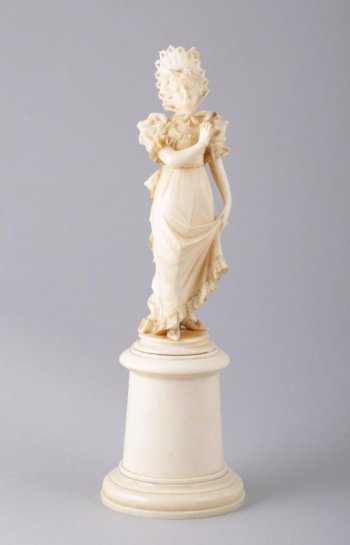 На высоком круглом постаменте изображена женская фигура в длинном платье с пышными короткими рукавами, на голове шляпка, завязанная под подбородком лентой. Левой рукой женщина поддерживает платье, правая рука - на уровне груди.