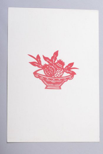 Вырезка из красной бумаги, наклеенная на белую. Вырезаны стилизованные фрукты с листьями в вазочке. Вазочка - конусообразная, низкая.