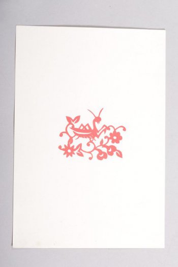 Вырезка из красной бумаги, наклеенная на белую. Вырезан кузнечик, сидящий на веткае цветка.