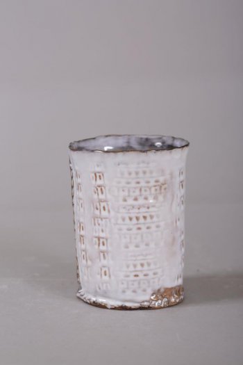 ваза цилиндрической формы с рельефным геометрическим орнаментом по тулову. Края горловины неправильной волнообразной формы, слегка оттянуты. Полива белая.