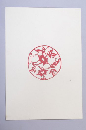 Вырезка из красной бумаги, наклеенная на белую. Вырезано растение с двумя цветами, листьями и ягодами в круге.
