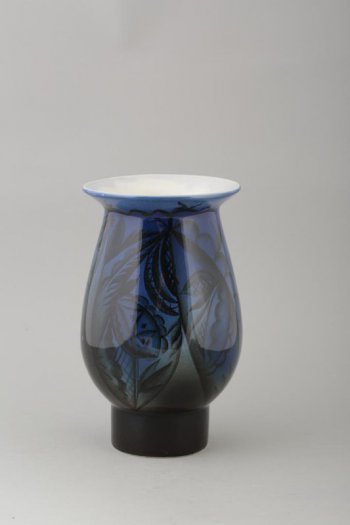 Округлое тулово вазы, расширенное книзу, переходит в высокую цилиндрическую ножку, горловина отогнута бортиком, тулово декорировано темно-синим цветом.
