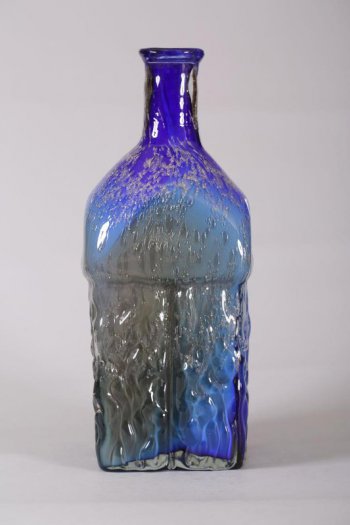 ваза вытянутой четырехугольной формы с длинной узкой горловиной  (ввиде бутылки), из темно-синего стекла, переходящего в фиолетовый, голубой, желтовато-зеленый, золотистый цвета. Нижняя часть вазы рельефная.