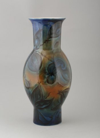 Округлое тулово вазы переходит в цилиндрическое основание и высокую горловинус отогнутым краем. Ваза декорирована крупным растительным орнаментом, выполненным черной краской на фоне сине-коричневых и зеленоватых пятен.