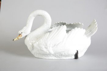 Сосуд в форме белого плывущего лебедя с приподнятыми крыльями, его шея изогнута, голова вытянута вперед.