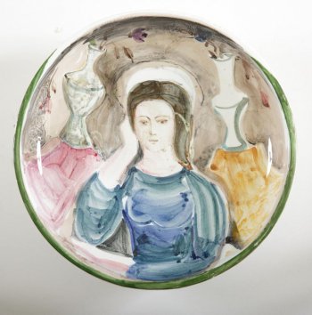 блюдо круглое, глубокое, на кольцевой ножке. В центральной части - погрудное изображение сидящей женщины в синем платке. Фон цветной с изображением двух ваз.