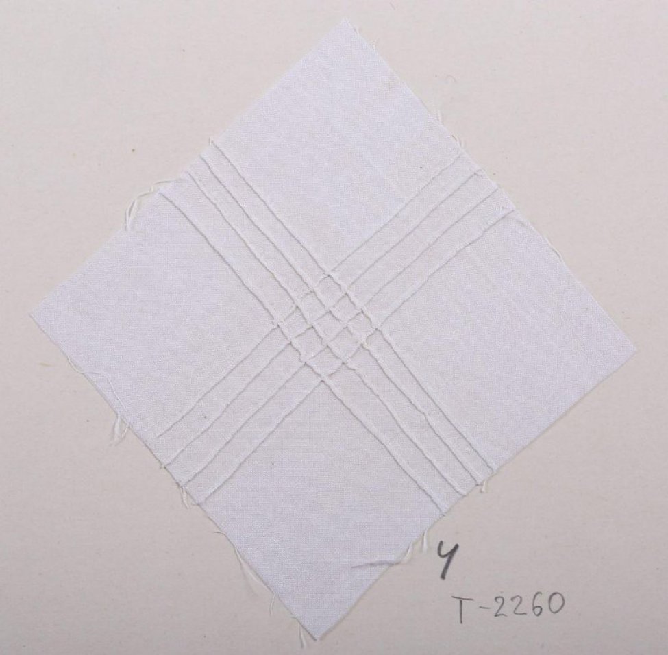 Образец квадратной формы белого цвета. По четыре ряда очень узких складочек шиты крест-накрест. В цнтре они пересекаются, образуя решотку. Образец приклеен на картонный лист.
