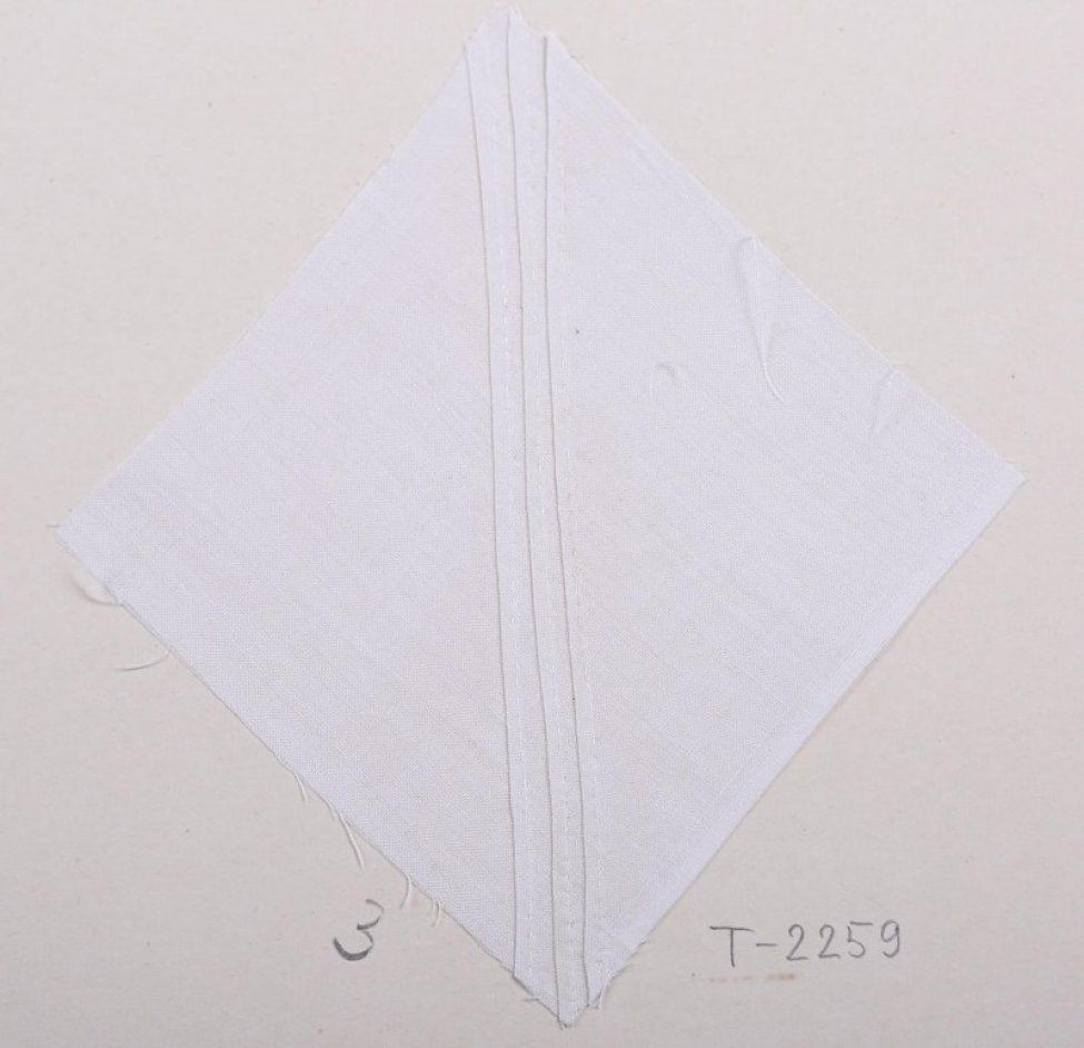 Образец в виде ромба белого цвета. По диагонали, снизу вверх белыми нитями шиты три прямые узкие складки. Образец приклеен на картоный лист.