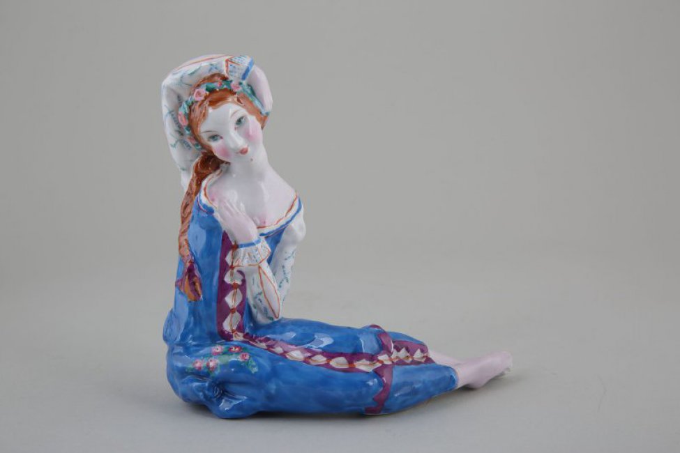 Изображена фигура сидящей балерины  в синем сарафане, с рыжей косой и венком на голове. Правая ее рука закинута за голову; левая - прижата к груди.