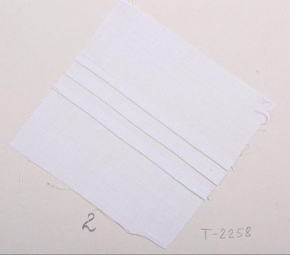 Образец квадратной формы белого цвета.  По середине образца тремя прямыми рядами шиты складки глубиной  0,4 - 0,5 см. Образец приклеен к картонному листу.