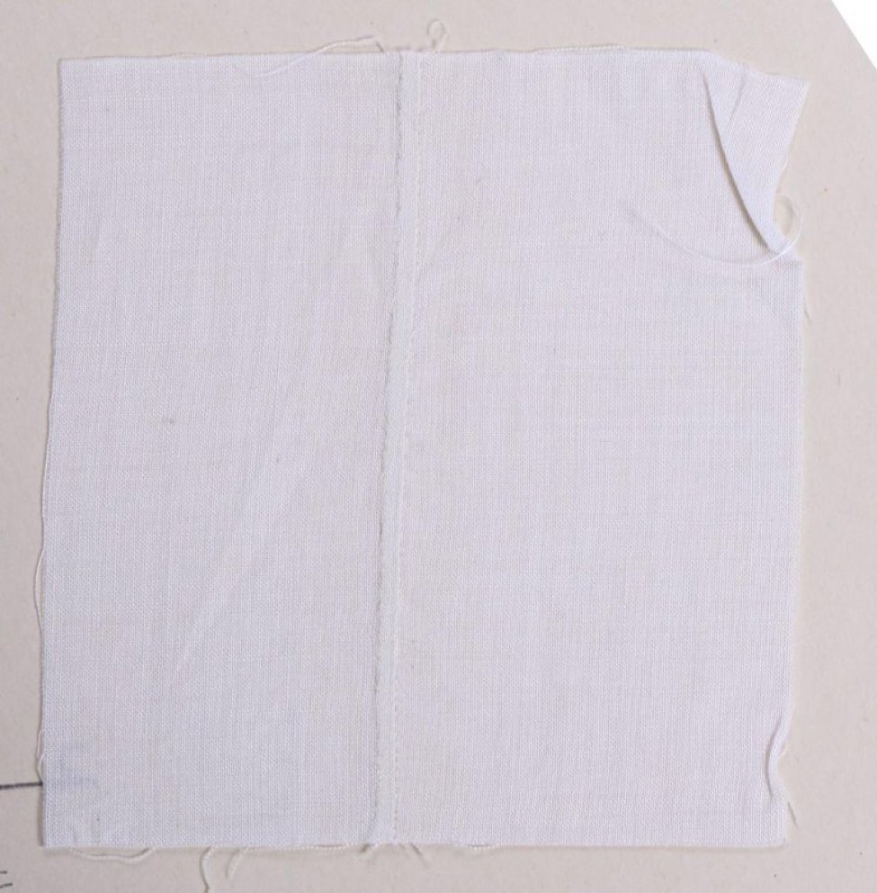 Образец квадратной формы белого цвета. По середине образца выполнен шов, создающий узкую рельефную зашитую складку. Образец не прикреплен к картонному листу.