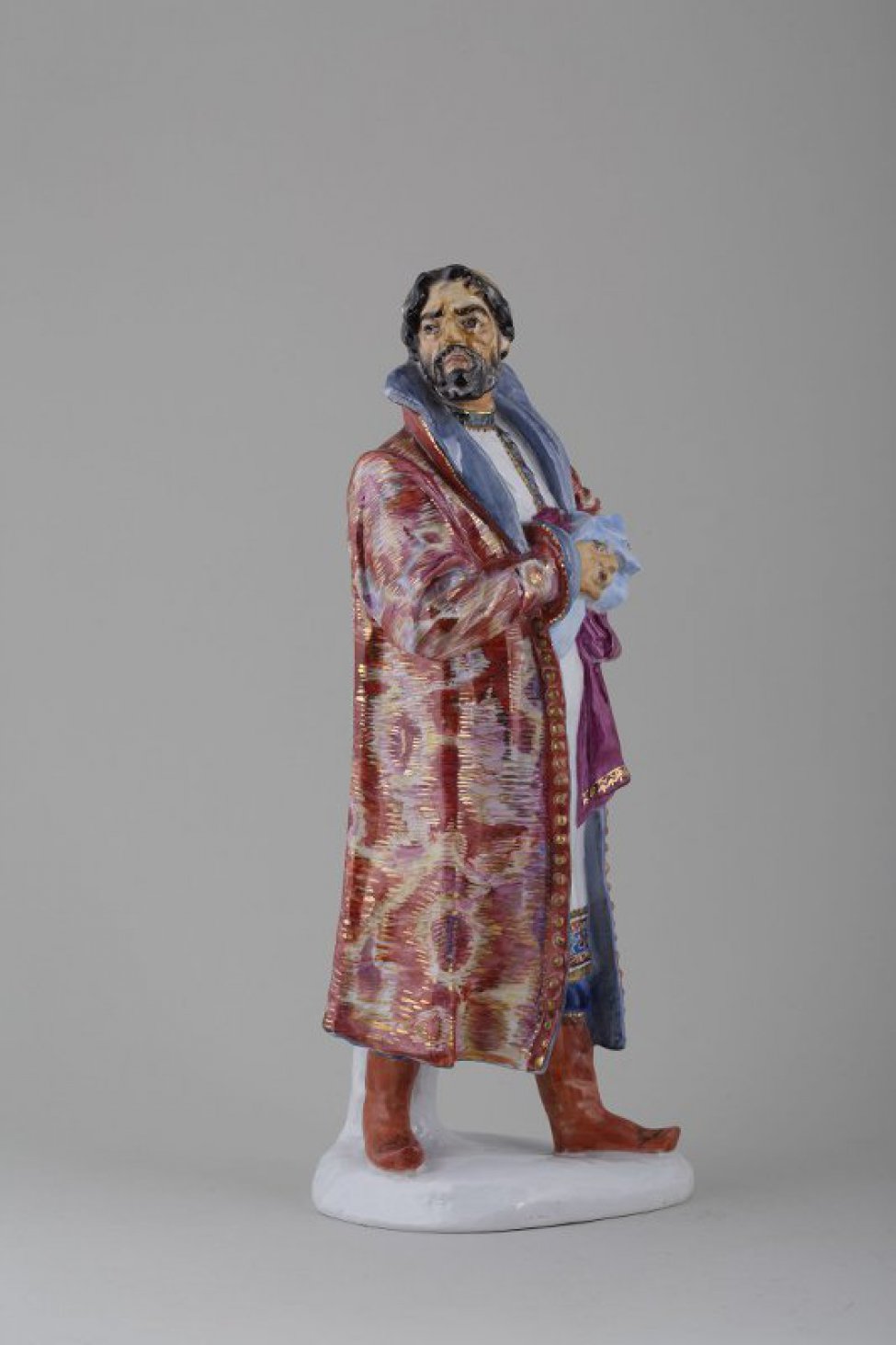 На невысоком основании фигура мужчины в царском костюме 16 века. На нем длинная, с орнаментом, белая рубаха; сверху - узорный кафтан; на голове круглая шапка; в руках, прижатых к груди, два платка.