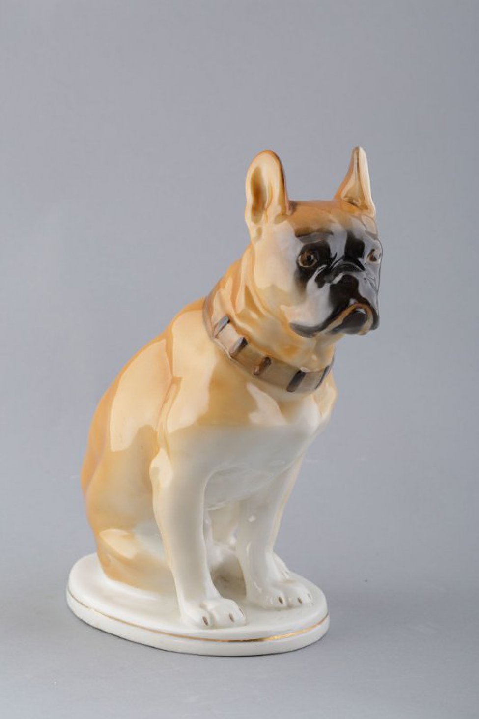 Фигура собаки, в ошейнике, сидящей на правом бедре с поджатыми задними лапами и опирающейся на передние лапы. Основание овальное, белое, с золоченой отводкой по середине.