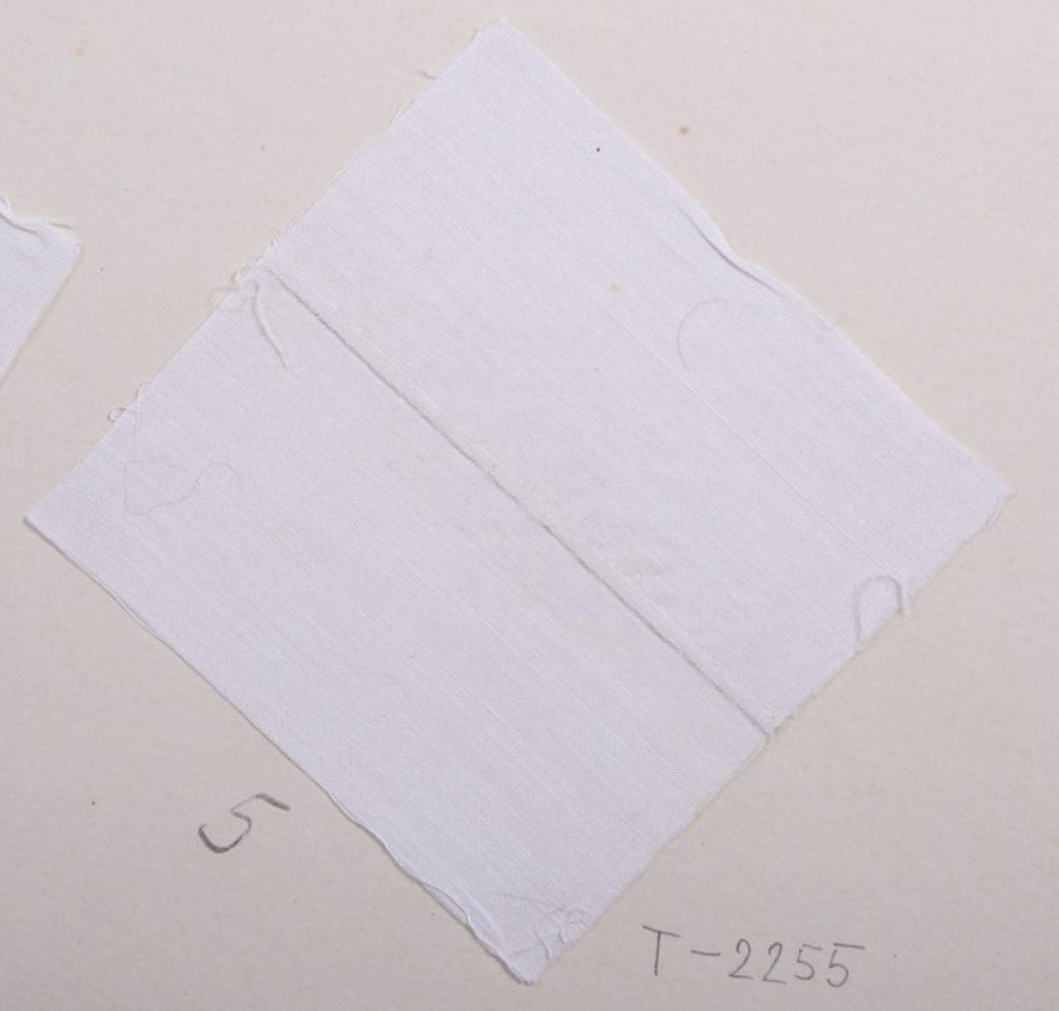 Образец квадратной формы белого цвета. По середине образца выполнен шов, содающий узкую рельефную зашитую складку. Образец приклеен на картонный лист.