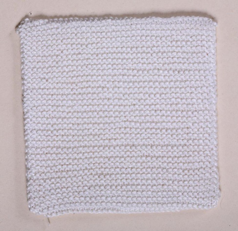 Образец квадратной формы из белых нитей  выполнен в технике вязки изнаночными петлями. Образец натянут на картонку и пришит на картонный лист.