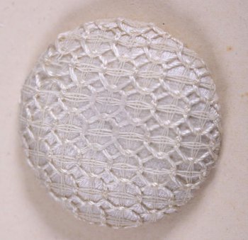 Пуговица круглой выпуклой формы, обтянутая белым атласом, на котором вышита сетка из овалов. Пуговица пришита к картонному листу.