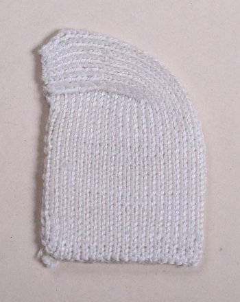 Образец прямоугольной, закругленной с одного угла формы из белых нитей  выполнен в технике вязки лицевыми петлями. Образец демонстрирует вязание пятки чулка или носка.