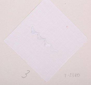 На белом батисте квадратной формы в центре дан образец последовательности выполнения шитья гладью. Образец в виде четырех фестонов с полуовалом на конце. Образец приклеен к картонному листу.