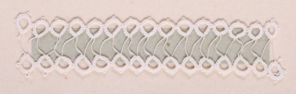 Образец белого цвета в виде двух узких полосок мелких колец соединенных между собой тонкой нитью. Образец пришит к картонному листу.