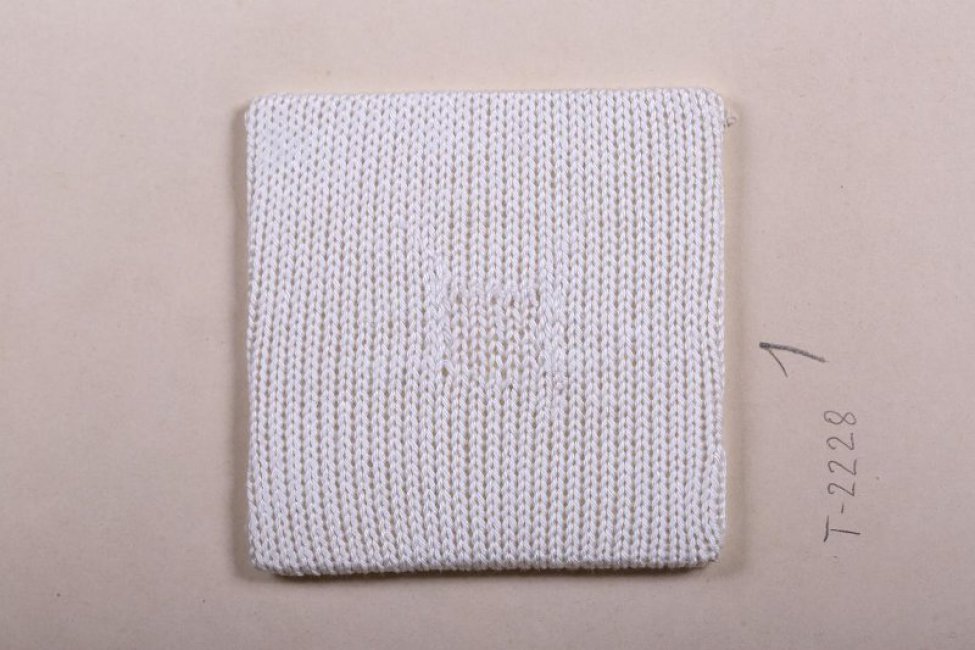 Из белых нитей связан образец квадратной формы лицевыми петлями. в центре его такими же нитями и лицевыми петлями выполнена ручная штопка.